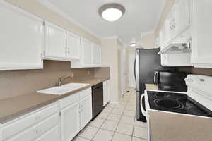 Kitchen featuring black appliances, white cabinets, ornamental molding, light tile patterned floors, and light countertops