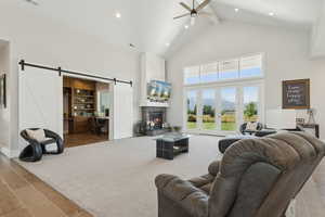 Living room with a barn door, a large fireplace, wood finished floors, a ceiling fan, and recessed lighting