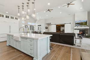 Kitchen with a barn door, vaulted ceiling, open floor plan, white cabinetry, and a glass covered fireplace