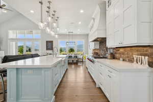 Kitchen with hanging light fixtures, a breakfast bar area, white cabinets, light stone counters, and glass fronted cabinets