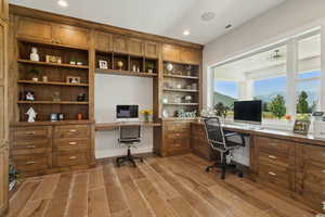 Office space with built in desk, recessed lighting, and light wood finished floors