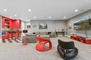 Living area with light carpet, recessed lighting, and bar with sink