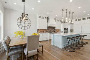 Kitchen with white cabinets, a breakfast bar, light wood finished floors, tasteful backsplash, and a large island