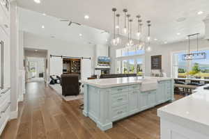Kitchen featuring a barn door, open floor plan, light wood-type flooring, decorative light fixtures, and light stone countertops