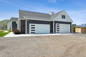 View of side of property featuring a mountain view, dirt driveway, and roof with shingles