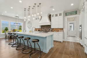 Dual tone kitchen with a kitchen bar, an island with sink, dark wood finished floors, decorative light fixtures, and two tone cabinets