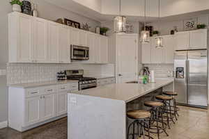 Kitchen featuring stainless steel appliances, white cabinets, a breakfast bar area, light stone countertops, and pendant lighting