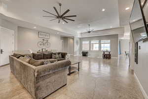 Living area with finished concrete flooring, a raised ceiling, a ceiling fan, and recessed lighting
