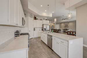 Kitchen featuring a large island with sink, white cabinets, ceiling fan, tasteful backsplash, and light stone countertops