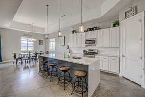 Kitchen featuring a tray ceiling, white cabinetry, stainless steel appliances, finished concrete flooring, and light stone countertops