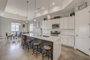 Kitchen with a tray ceiling, white cabinetry, stainless steel appliances, a kitchen breakfast bar, and concrete flooring