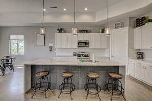 Kitchen featuring white cabinetry, light stone countertops, a breakfast bar, stainless steel appliances, and a raised ceiling