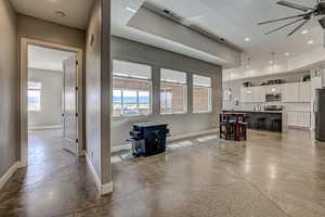 Interior space featuring finished concrete floors, a ceiling fan, stainless steel appliances, a kitchen island with sink, and pendant lighting