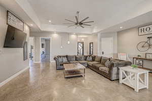 Living area featuring a ceiling fan, a tray ceiling, recessed lighting, and finished concrete floors