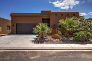 Pueblo revival-style home with an attached garage, stucco siding, and concrete driveway