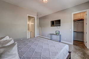 Bedroom featuring concrete flooring, a spacious closet, and ensuite bath