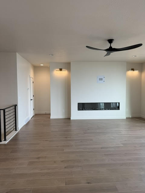 Unfurnished living room featuring wood finished floors, ceiling fan, a glass covered fireplace, and recessed lighting