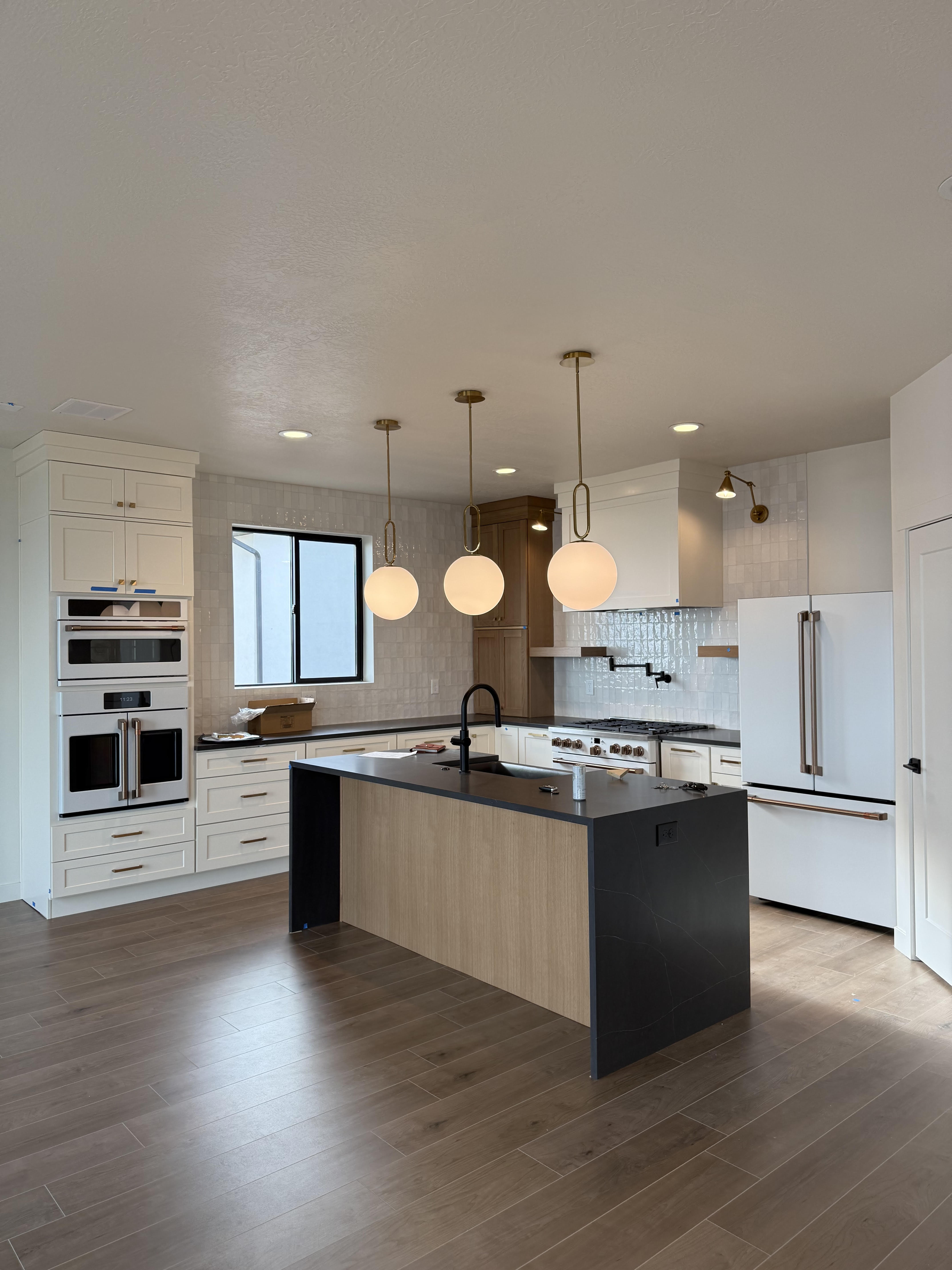 Kitchen featuring premium appliances, a kitchen island with sink, decorative backsplash, hanging light fixtures, and dark stone counters