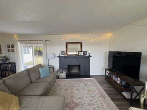Living room with dark wood-type flooring, a textured ceiling, and a fireplace