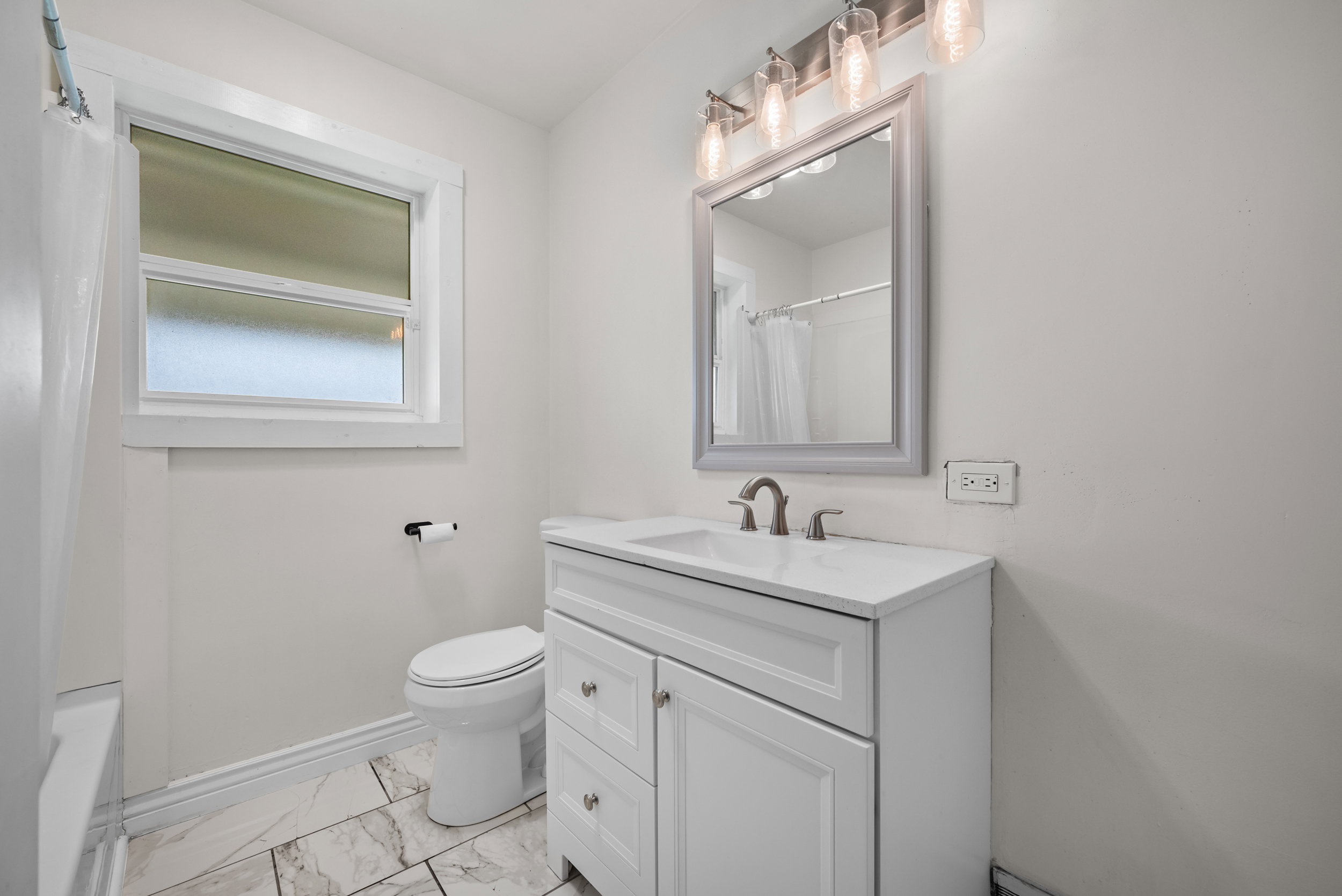Bathroom featuring a white vanity with an integrated sink, brushed nickel faucet, and a framed mirror with a four-light vanity fixture