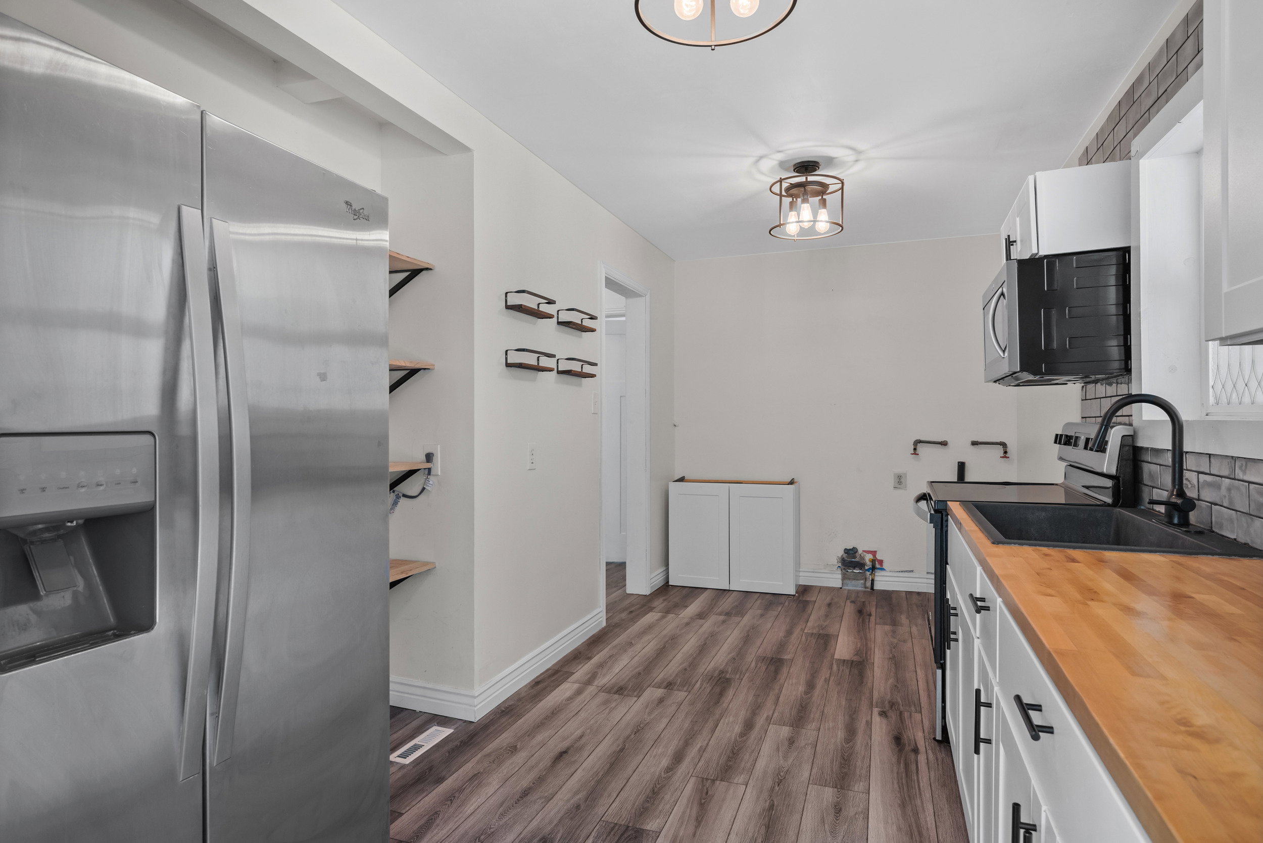 Kitchen featuring wood-finish flooring, white cabinetry with matte black hardware, butcher block countertops, and a black composite sink with a matte black faucet