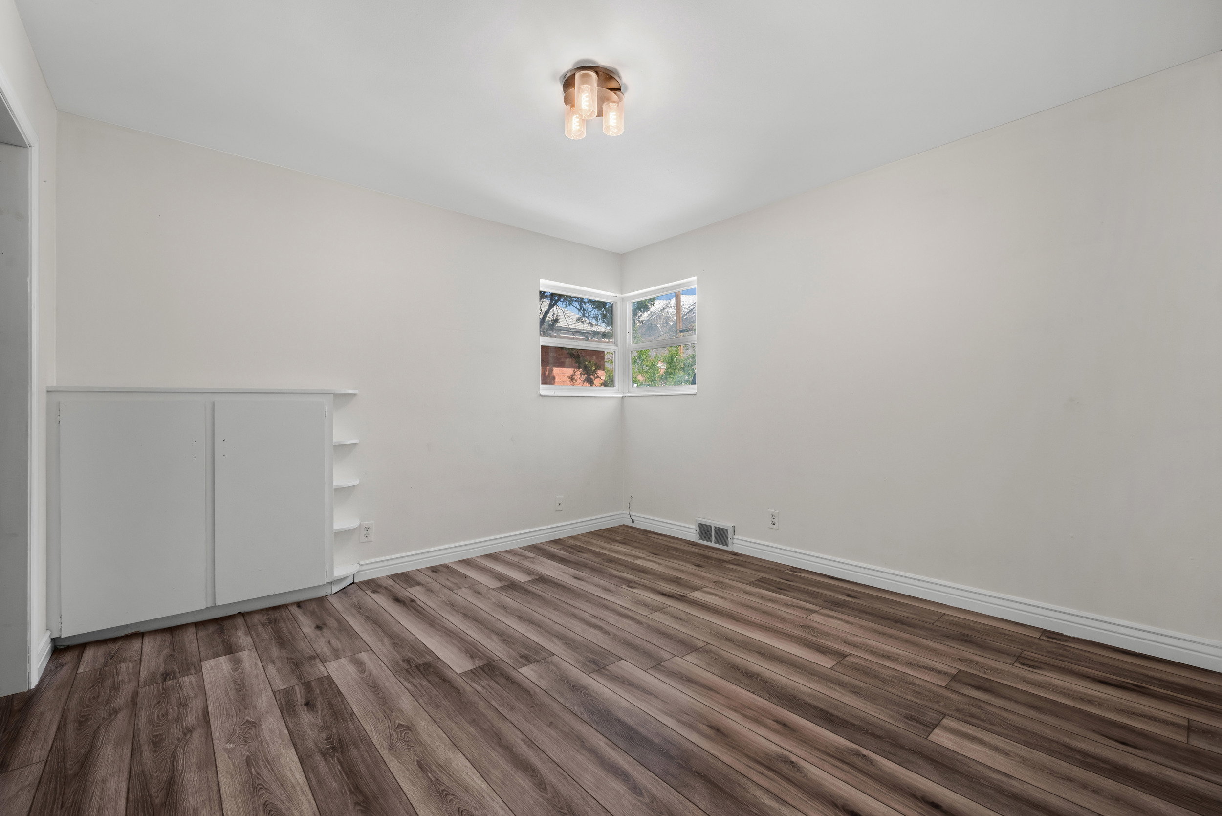 Room featuring rich wood-finish flooring, white baseboards, and a built-in white cabinet with open shelving