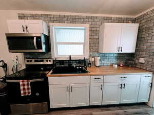 Kitchen featuring stainless steel appliances, white cabinetry, and wooden counters