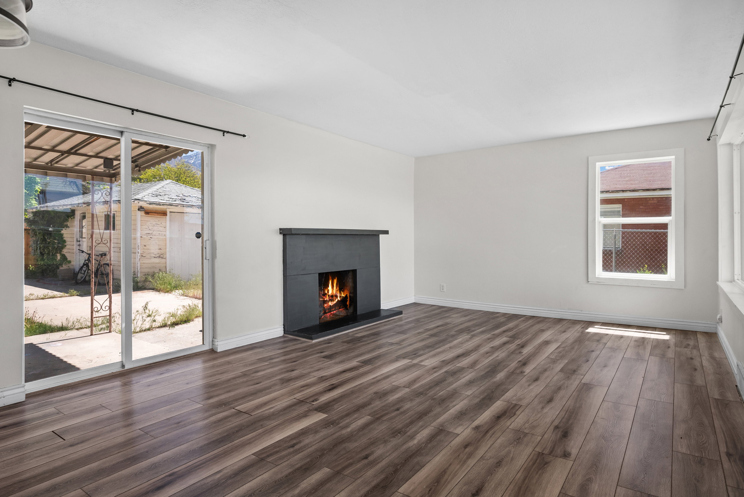 Living space featuring wood-finish flooring, a contemporary fireplace with a dark mantel, white baseboards, and a sliding glass door providing access to the exterior