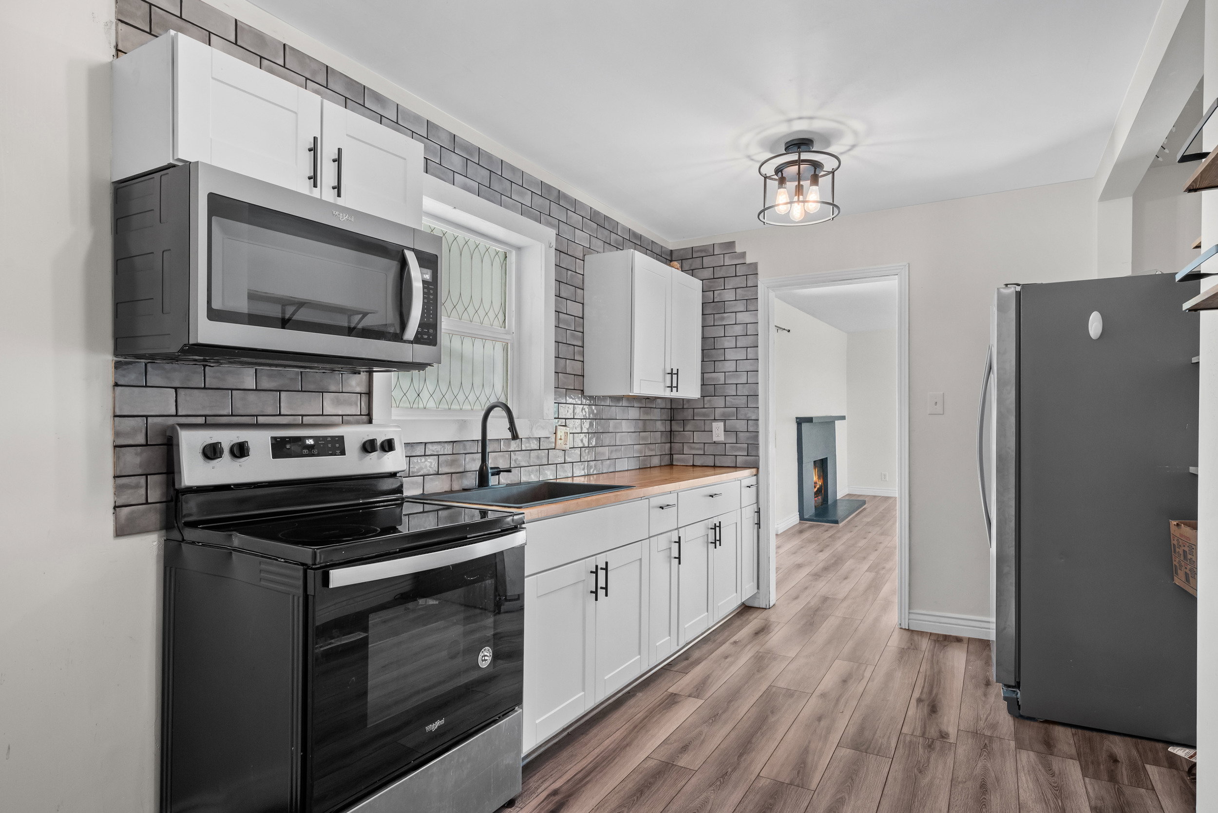 Kitchen featuring wood-finish flooring, white cabinetry with matte black hardware, a black subway tile backsplash, and butcher block-style countertops