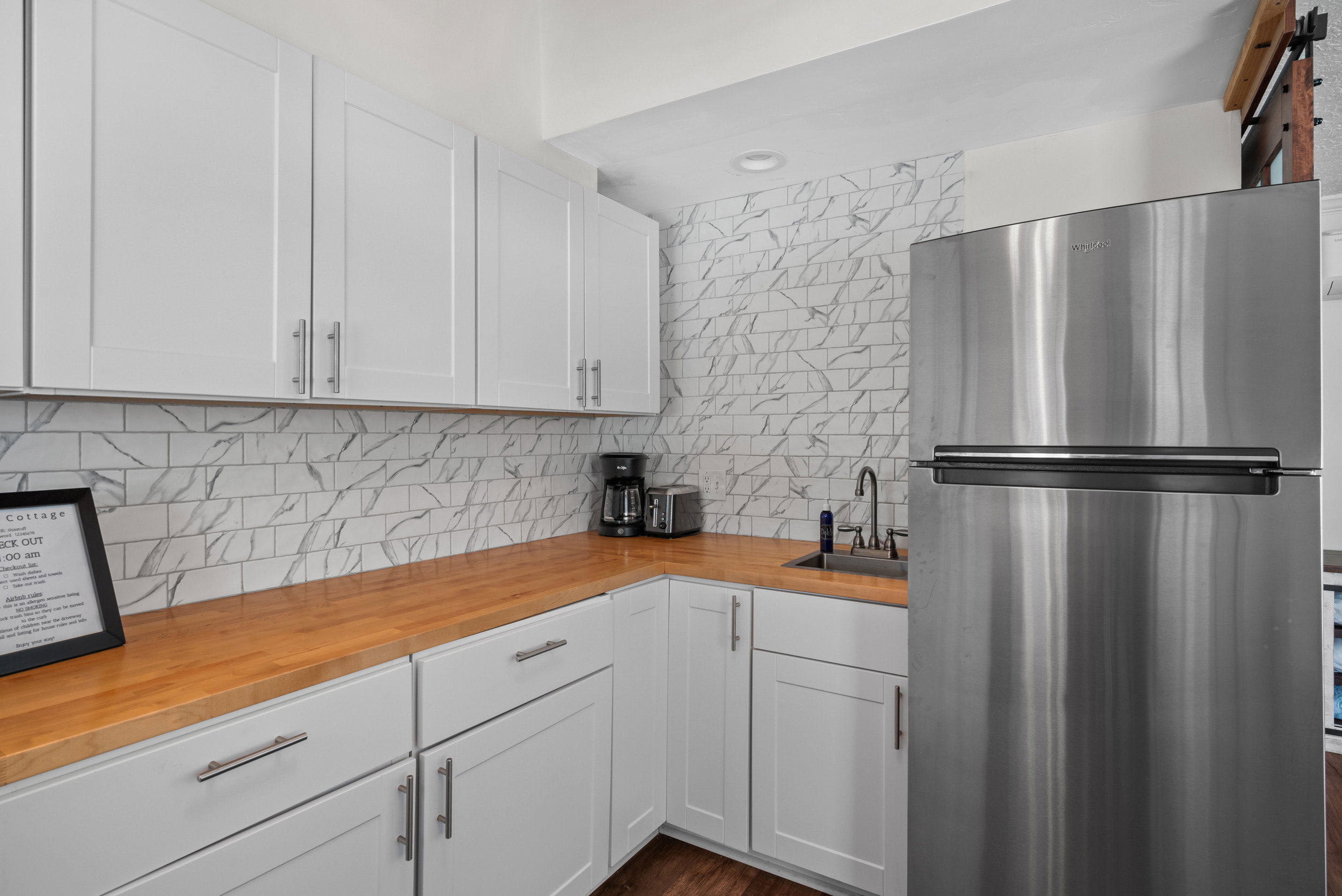 Modern kitchen featuring white shaker cabinetry, wood-finish countertops, stainless steel appliances, and a marble-look subway tile backsplash