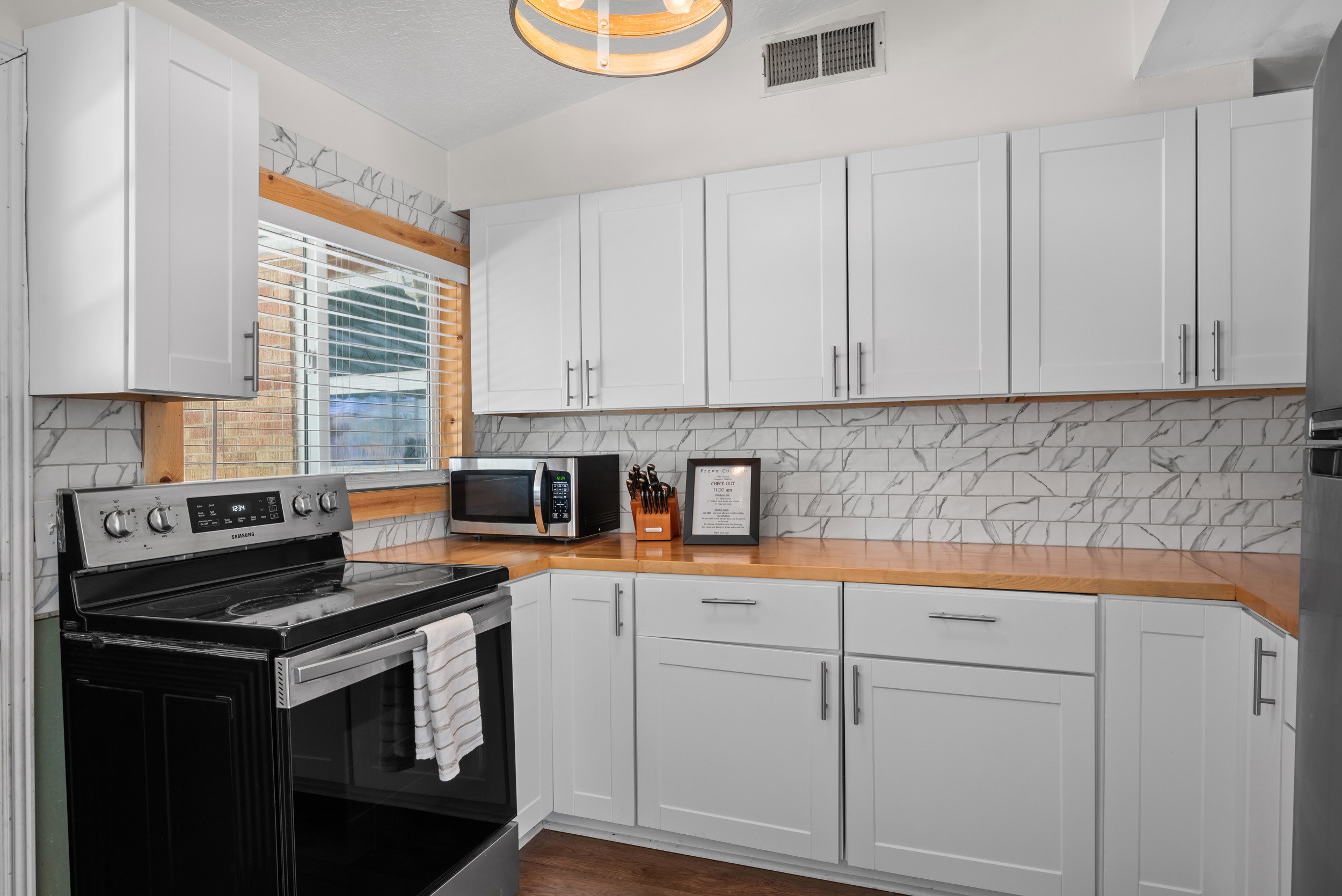 Modern kitchen featuring white shaker cabinetry, light wood-finish countertops, and a white subway tile backsplash with grey veining
