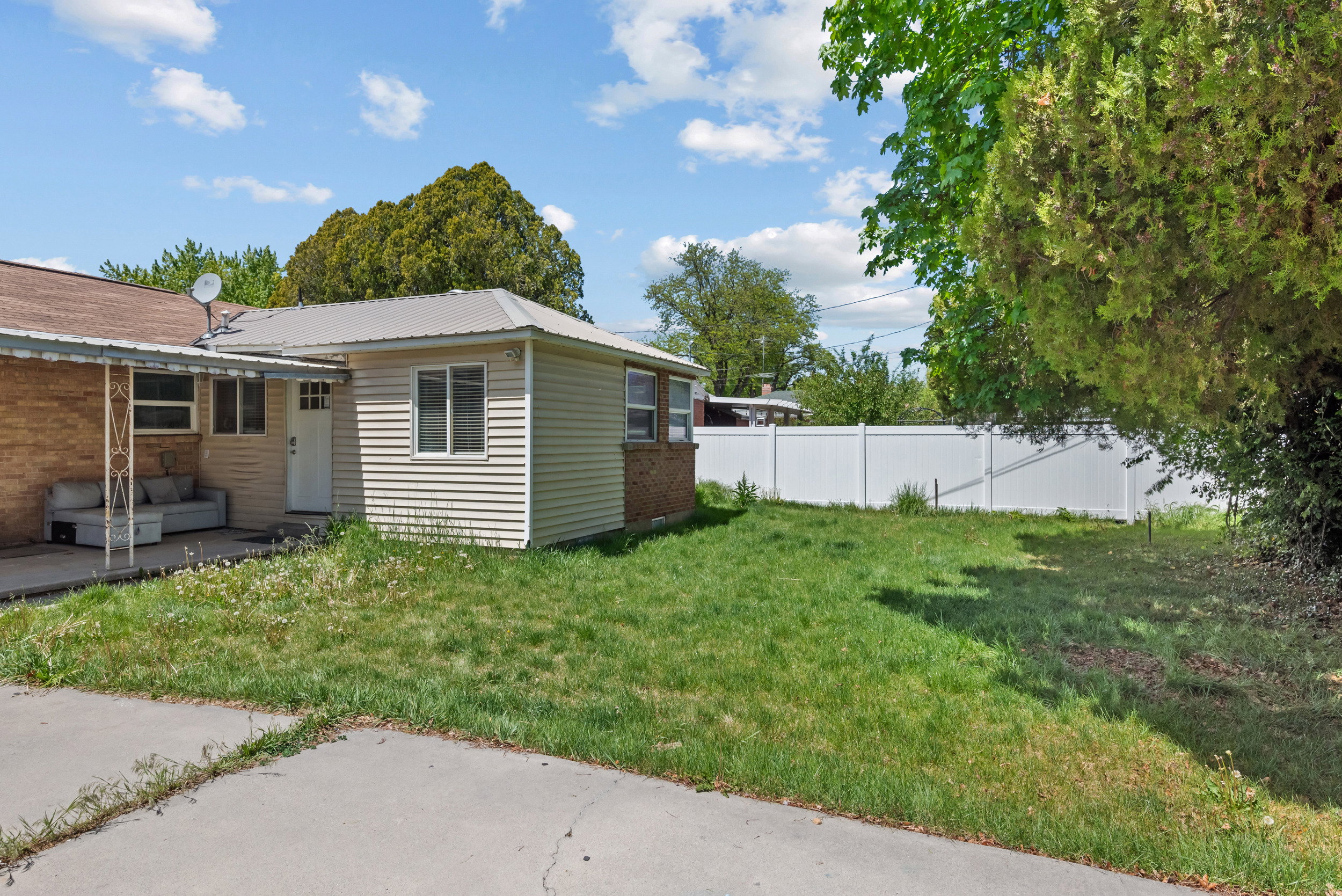 Rear exterior with a metal roof accent, vinyl siding, brick detailing, a white entry door, and a covered concrete patio