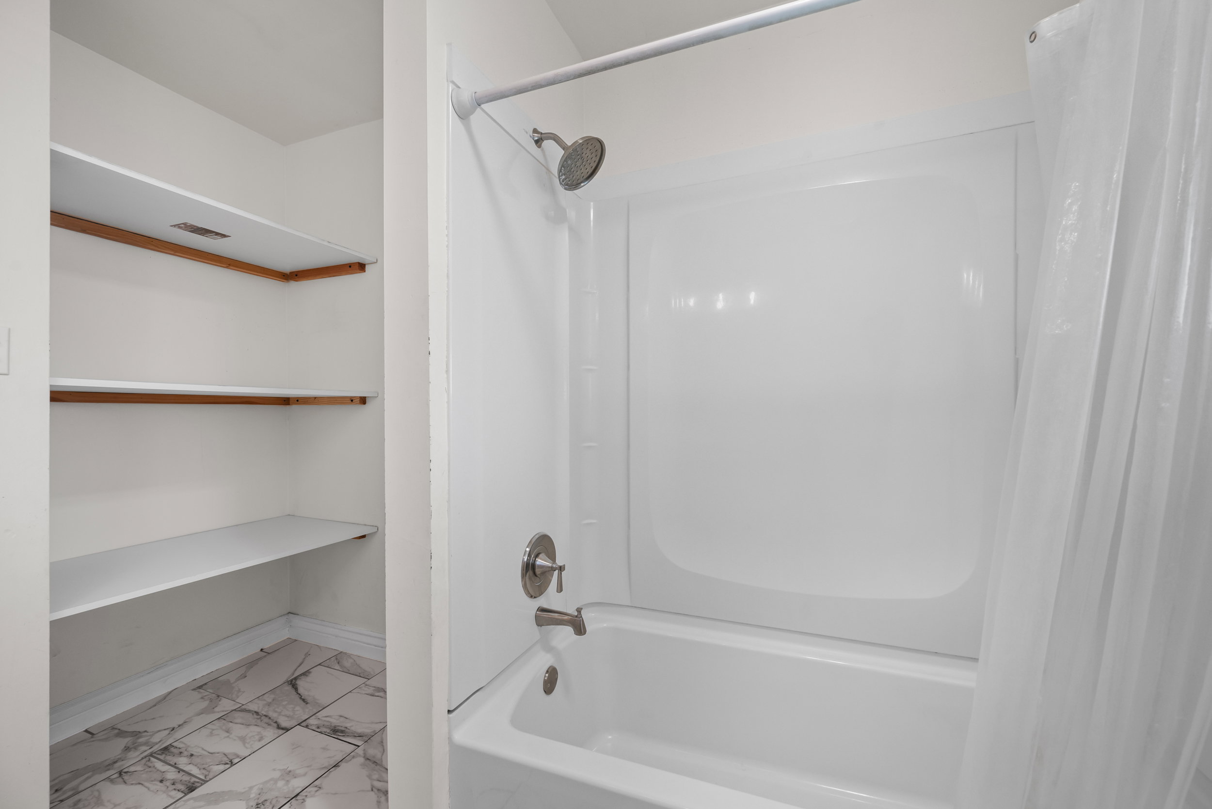White bathtub with an integrated shower, featuring a brushed nickel showerhead and faucet