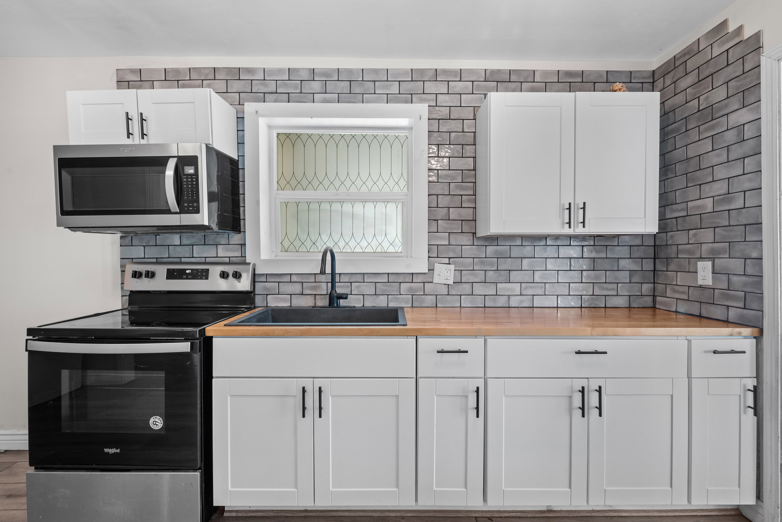 Modern kitchen featuring white shaker-style cabinetry with matte black hardware, butcher block countertops, and a subway tile backsplash