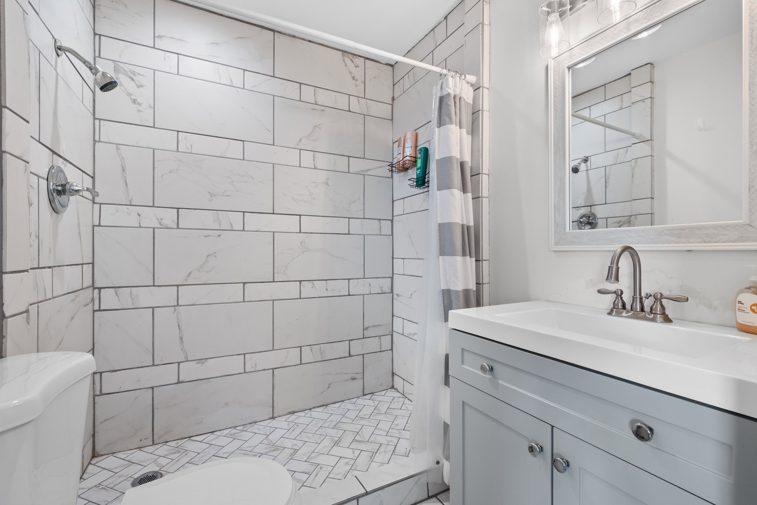 Tiled shower enclosure featuring white subway-style tiling with gray veining and a herringbone pattern on the shower floor