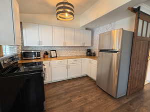 Kitchen with stainless steel appliances, white cabinetry, butcher block countertops, tasteful backsplash, and dark wood-style floors