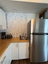 Kitchen with freestanding refrigerator, white cabinets, decorative backsplash, and wooden counters