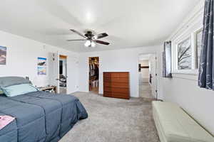 Bedroom featuring light colored carpet, a walk in closet, and ceiling fan