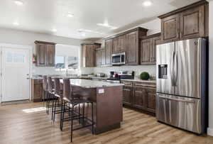 Kitchen featuring stainless steel appliances, a center island, light wood-style flooring, a breakfast bar area, and dark wood finish cabinets