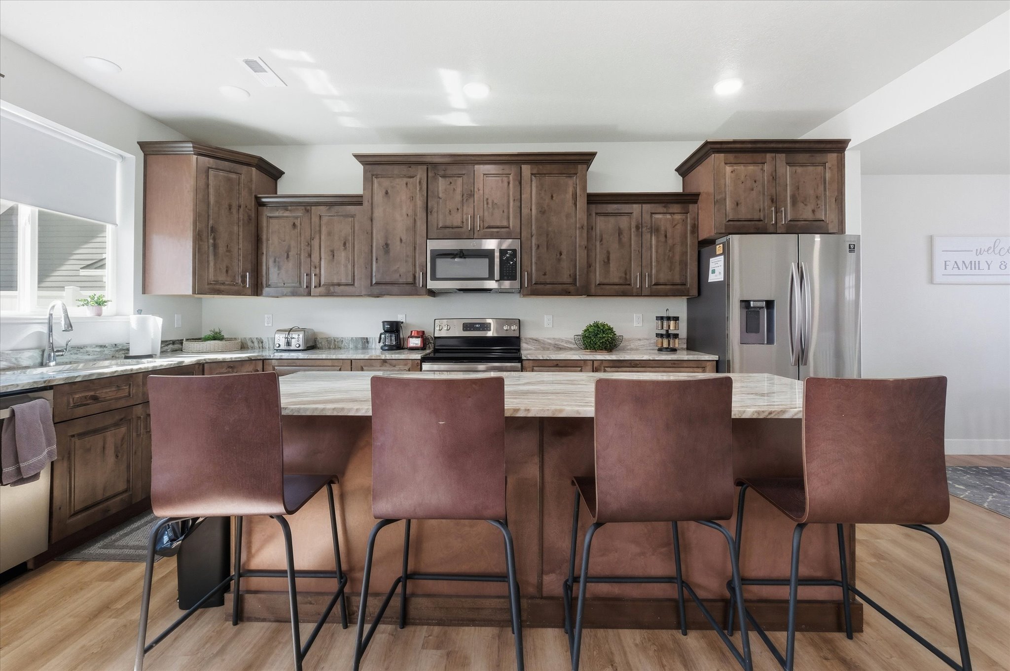 Kitchen with stainless steel appliances, dark wood finish cabinets, light stone countertops, light wood-style floors, and recessed lighting