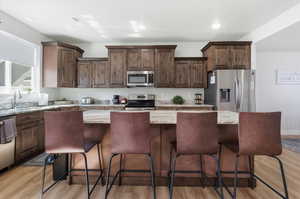 Kitchen with stainless steel appliances, dark wood finish cabinets, light stone countertops, light wood-style floors, and recessed lighting