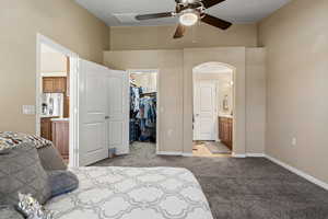 Bedroom with connected bathroom, a spacious closet, light colored carpet, and arched walkways