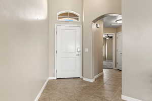 Foyer with arched walkways, a ceiling fan, and light tile patterned floors