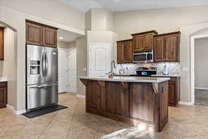 Kitchen featuring arched walkways, stainless steel appliances, a breakfast bar, light tile patterned floors, and light stone counters