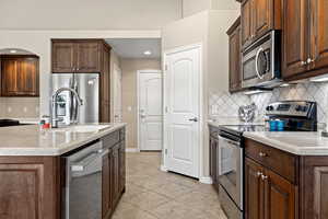 Kitchen featuring stainless steel appliances, dark wood finish cabinets, backsplash, light stone counters, and recessed lighting
