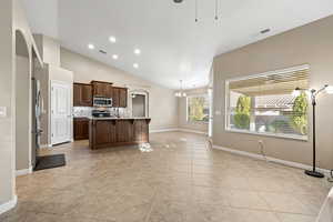 Kitchen with light countertops, a kitchen breakfast bar, an island with sink, dark wood finish cabinetry, and lofted ceiling