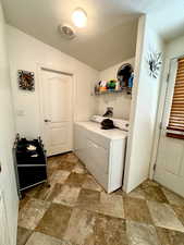 Laundry room with a textured ceiling, stone finish flooring, and washing machine and dryer