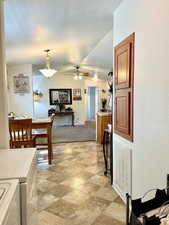 Dining area with ceiling fan, vaulted ceiling, stone finish floors, and washing machine and clothes dryer