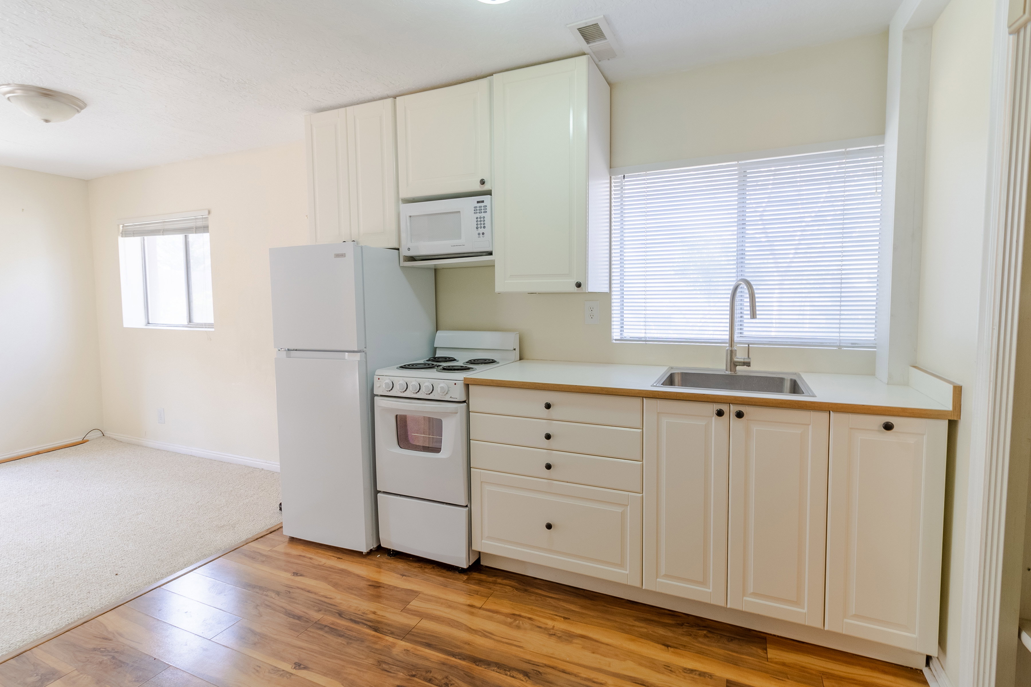 Kitchen with white appliances, light countertops, white cabinetry, light wood-type flooring, and light colored carpet