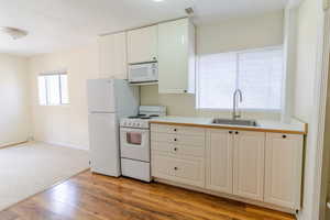 Kitchen with white appliances, light countertops, white cabinetry, light wood-type flooring, and light colored carpet